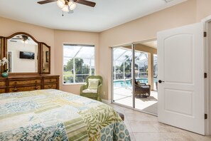 Ein Schlafzimmer mit einem großen Bett, einem Schminktisch, einem Sessel und einer Tür, die auf einen Balkon mit einem Pool führt.