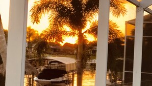 Vista a través de una ventana de un puerto deportivo con barcos, palmeras y un atardecer.