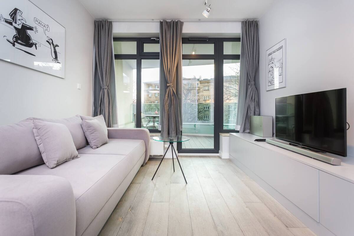 A modern living room with a sofa, a TV, and a balcony with curtains.