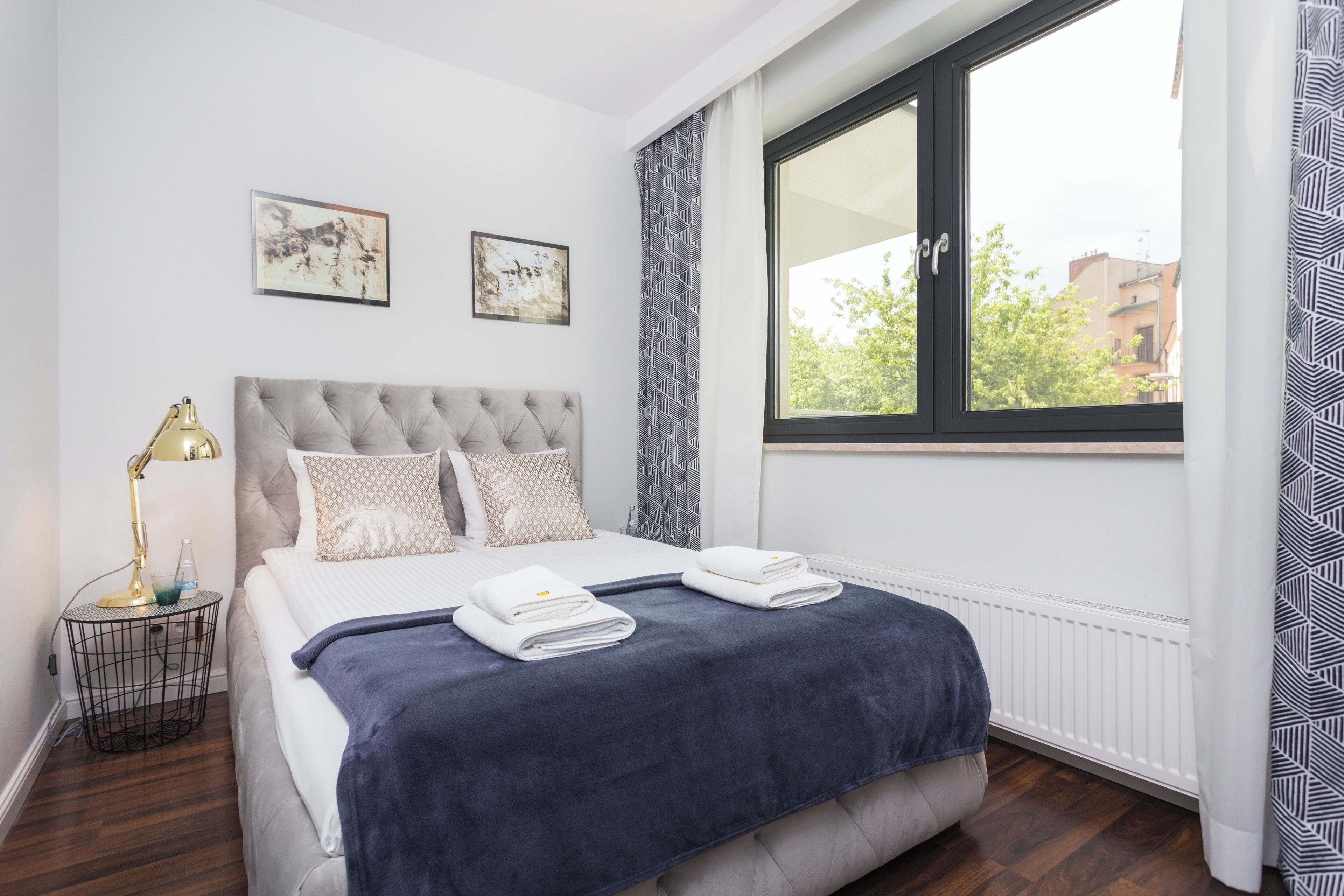 A neatly made bed with a dark blue blanket, a bedside lamp, and two framed artworks on the wall.