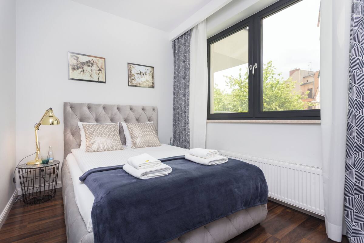 A neatly made bed with a dark blue blanket, a bedside lamp, and two framed artworks on the wall.