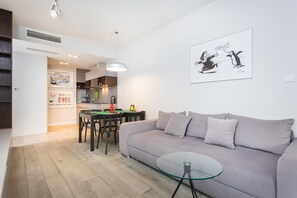 Uma sala de estar moderna com um sofá cinzento, uma mesa de centro de vidro e um espaço de jantar com uma mesa e cadeiras.