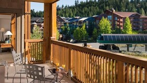 Een balkon met houten hekwerk, een tafel met stoelen en uitzicht op een resort met gebouwen en bomen.