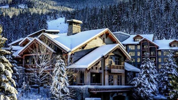 Een groot landhuis met meerdere gebouwen, omringd door besneeuwde bomen en bergen.