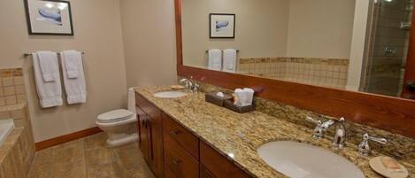 A bathroom with a granite countertop, two sinks, a mirror, and a toilet.