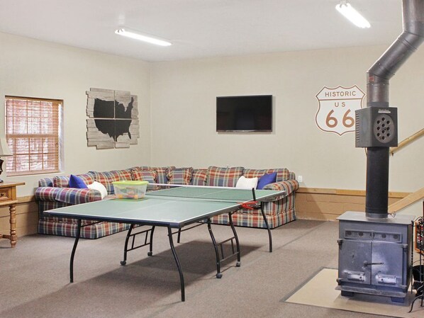 A living room with a ping pong table, a sofa, a television, and a wood-burning stove.