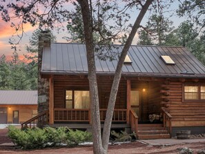 A log cabin with a porch, a chimney, and a metal roof.