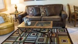 Ein Wohnzimmer mit einem braunen Ledersofa, gemusterten Kissen, einem Couchtisch mit einem geometrischen Teppich und drei Landschaftsbildern an der Wand.