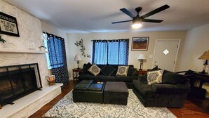 A living room with a fireplace, a ceiling fan, and a large window with blinds. - NEW! Walk to Old Littleton and light rail from this lovely home w/private yard (Littleton)