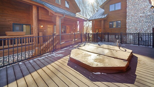 A wooden cabin with a stone wall, a wooden deck, and a metal railing.