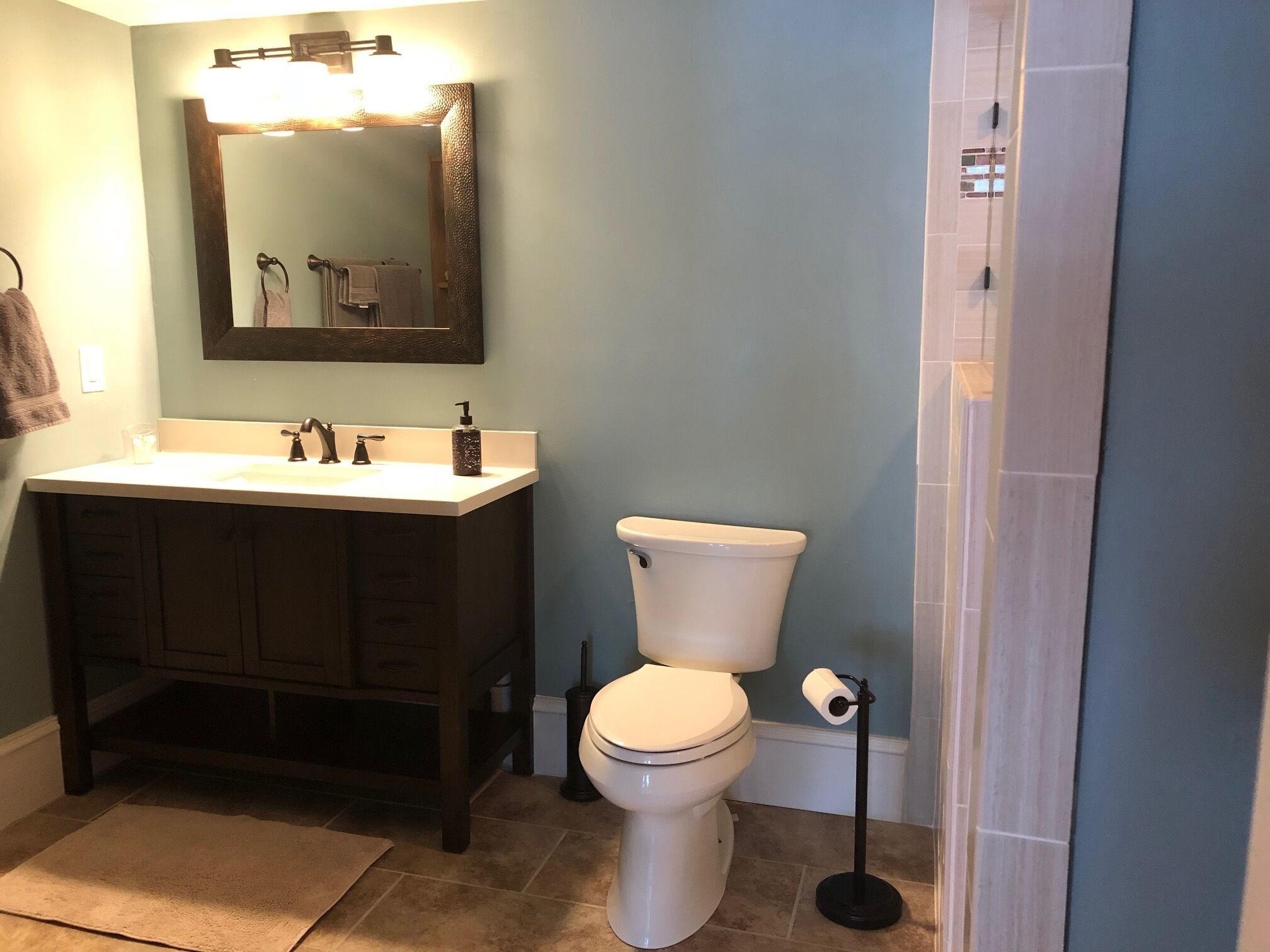 A bathroom with a sink, mirror, toilet, and a shower area.