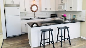 A kitchen with white cabinets, a black countertop, a central island with stools, a microwave, a toaster, and a pendant light.