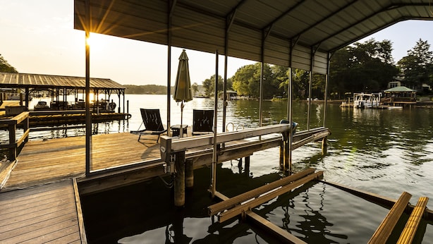 A covered dock with wooden benches and tables, a metal railing, and a view of the water and distant buildings.