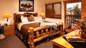 A bedroom with a wooden bed, two bedside lamps, a painting on the wall, and a view of the outdoors through a window. - Ski-in Condo | Wood Fireplace, Balcony (Beaver Creek)