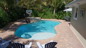 A swimming pool with a basketball hoop, surrounded by palm trees and a patio area with chairs. - Well Appointed Home Salt Water Pool & Separate Pool House & Putting Green (Hobe Sound)
