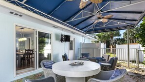 A covered patio area with wicker furniture, a round table, and a ceiling fan. - Well Appointed Home Salt Water Pool & Separate Pool House & Putting Green (Hobe Sound)