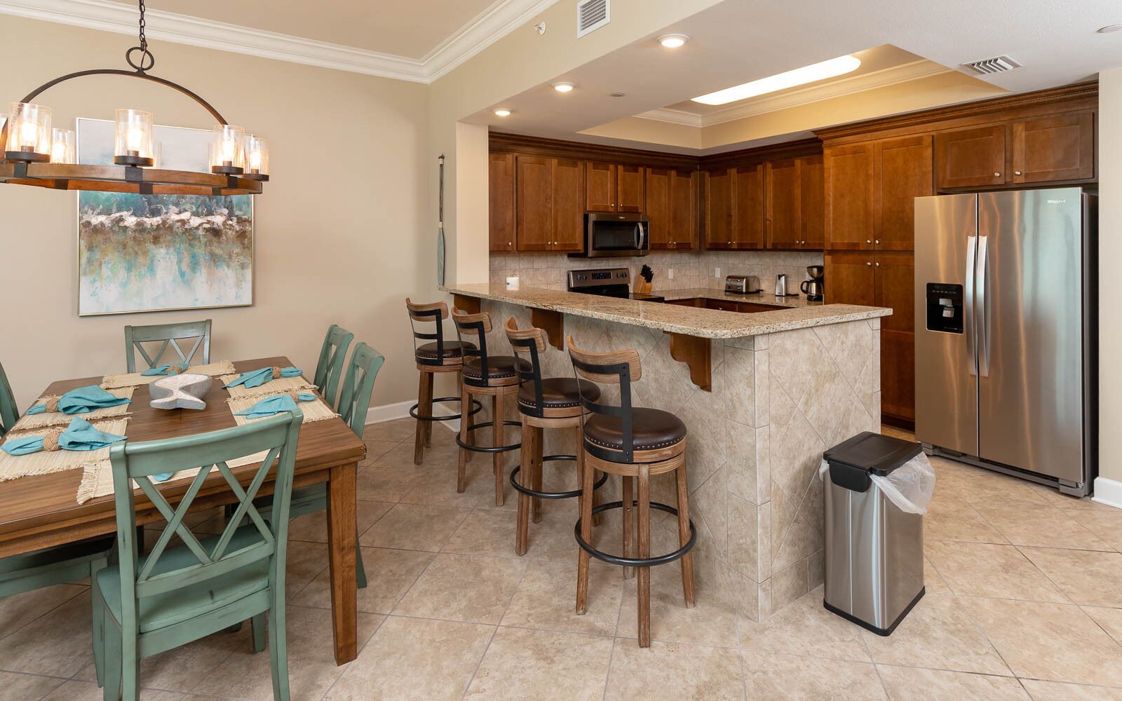 A kitchen with wooden cabinets, a stainless steel refrigerator, a microwave, and a dining area with a table and chairs.