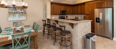 A kitchen with wooden cabinets, a stainless steel refrigerator, a microwave, and a dining area with a table and chairs.