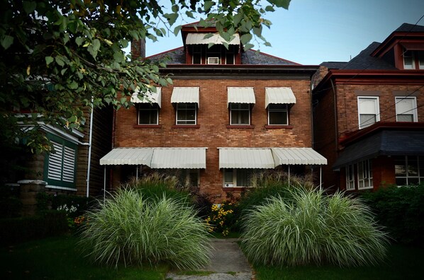 A brick building with a central entrance, large windows with awnings, and a pathway leading to the entrance.