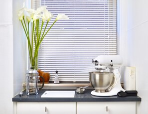 A kitchen counter with a stand mixer, a bowl, a cutting board, and a vase with flowers.