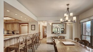 A spacious kitchen with wooden cabinets, a bar area, and a dining room with a large wooden table and chairs. - Premier Slopeside Apartment | Fireplace (Breckenridge)
