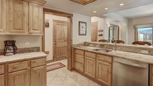 A kitchen with wooden cabinets, granite countertops, a built-in dishwasher, and a window with a city view. - Premier Slopeside Apartment | Fireplace (Breckenridge)