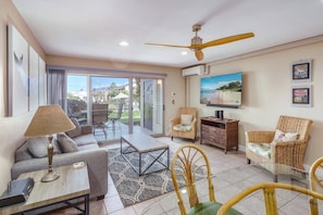 A spacious living area with a sofa, chairs, a coffee table, and a TV mounted on the wall. - Hale Kamaole 150 | Ground-Floor Ocean View, Lanai, King Bed, Split A/C, Sleeps 4 (Kihei)