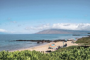 A beach with a rocky shoreline, a mountain in the background, and a clear sky.