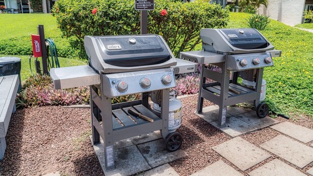 Zwei tragbare Gasgrills mit Bedienelementen, eine Gasflasche und ein Schild mit der Aufschrift 'Gasgrill starten'.