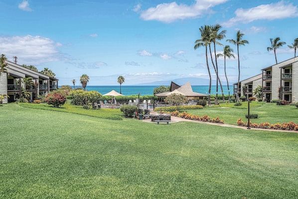 A resort with multiple buildings, a well-maintained lawn, and a view of the ocean.