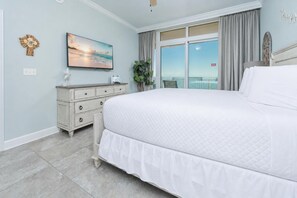 A bedroom with a large bed, a dresser, a painting, a plant, and a balcony with curtains.