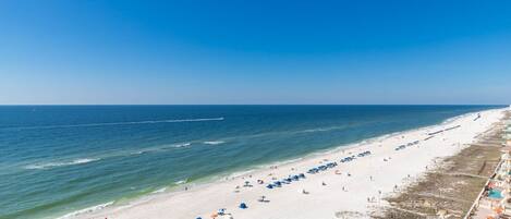 A beach with rows of umbrellas and a pool area.