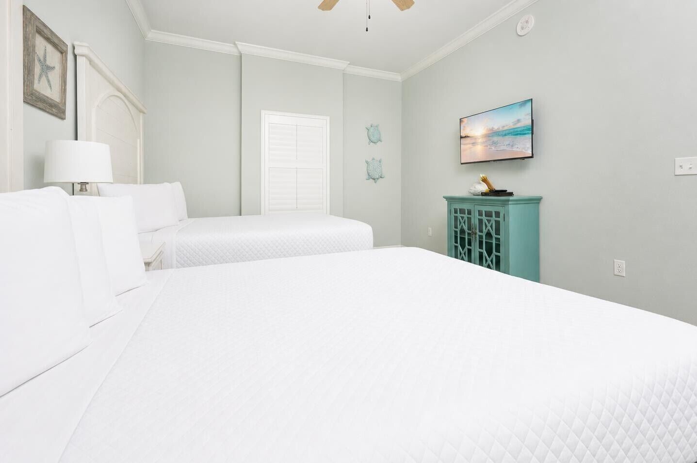 A bedroom with a large bed, a smaller bed, a teal cabinet, a TV, and a starfish decoration.