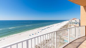 A beach view from a balcony with a railing, ocean, and beach umbrellas. - Stylish Oceanview Escape 3 BR 3 BA Phoenix Orange Beach 902 (Orange Beach)