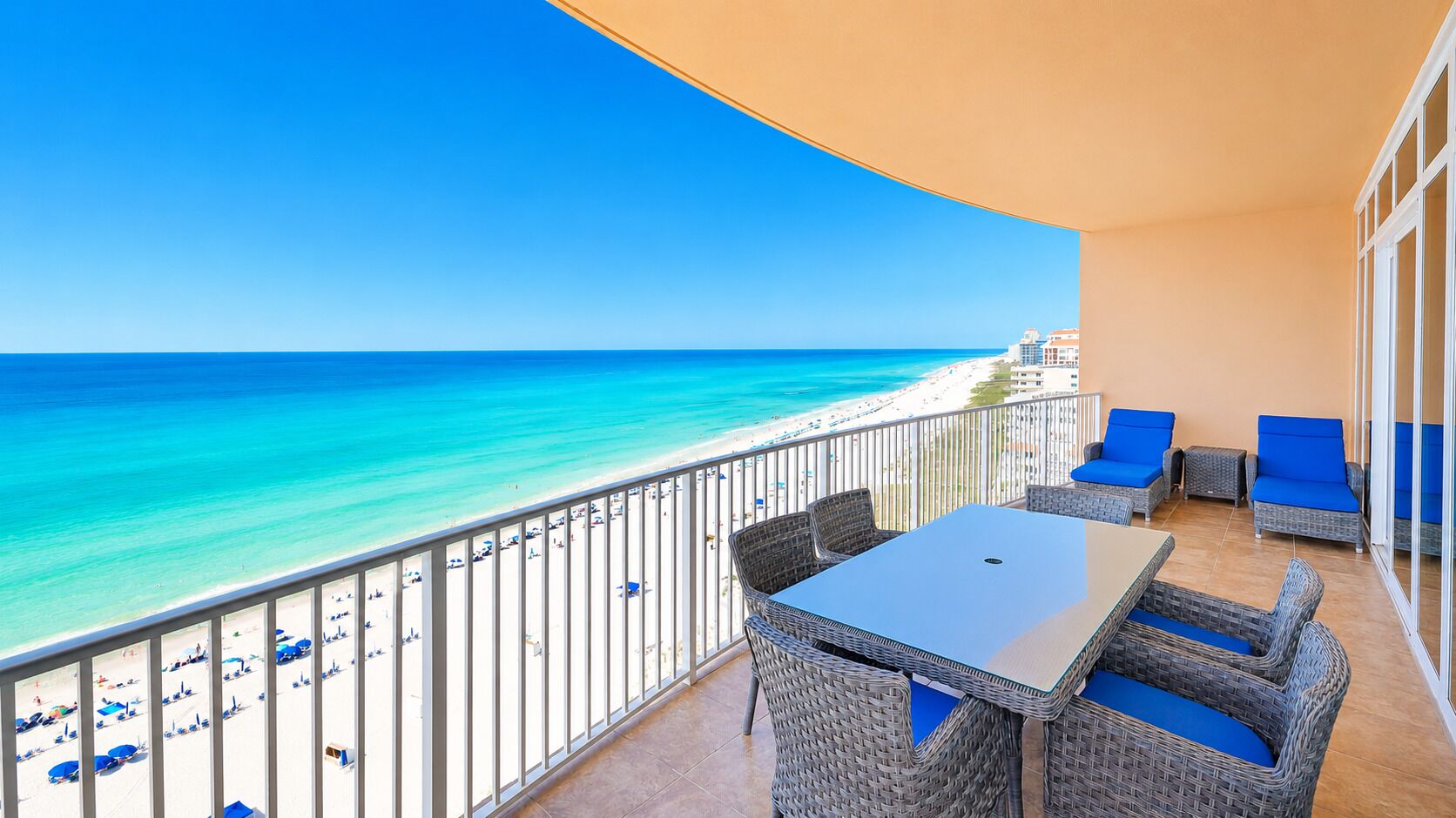 A balcony with a view of the beach and ocean, wicker furniture, and a table.