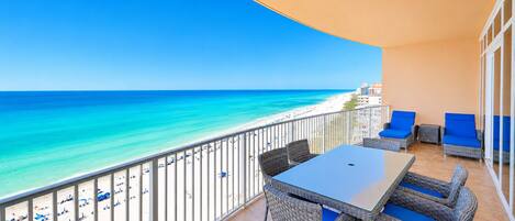 A balcony with a view of the beach and ocean, wicker furniture, and a table.