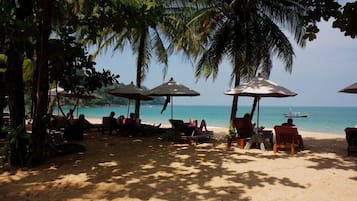 A beach with palm trees, sun loungers, and umbrellas.