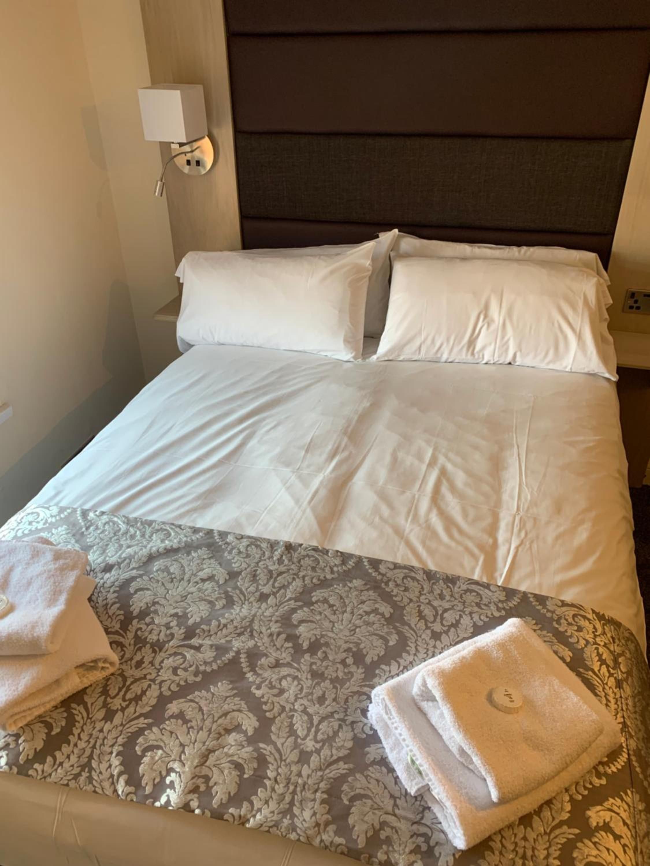 Una habitación de hotel con una cama bien hecha, una lámpara de noche y un enchufe en la pared.