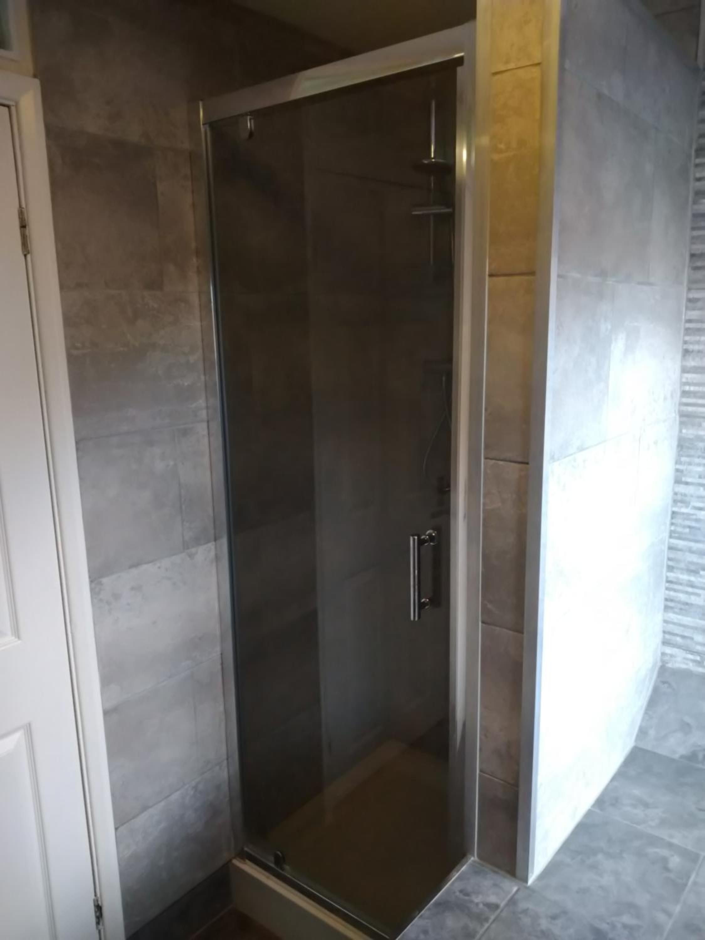 Un box de ducha con paredes de vidrio y puerta, junto a una puerta blanca y una pared con azulejos.