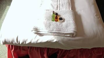 Un lit bien fait, avec du linge de lit blanc, une serviette pliée et deux flacons de produits de toilette posés sur une autre serviette blanche.