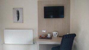 A hotel room with a bed, a desk with a kettle and a cup, a television mounted on the wall, and a radiator. - Wellington Hotel (Goole)