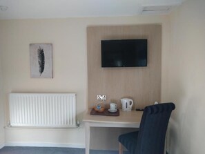 Une chambre d’hôtel comprenant un lit, un bureau avec une bouilloire et une tasse, un téléviseur fixé au mur et un radiateur.