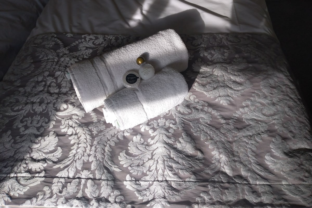 Una cama bien hecha con una colcha estampada y dos toallas blancas dobladas encima.