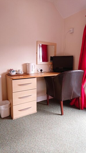 Une petite pièce, bien rangée, avec un bureau en bois, une chaise, un ordinateur portable, une bouilloire et une poubelle.