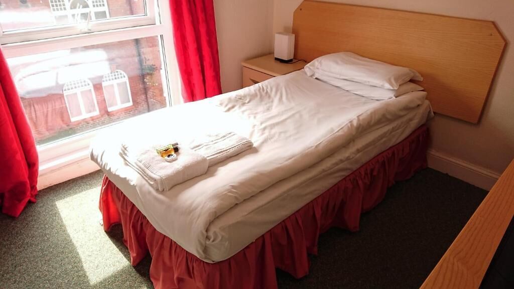 A single bed with a wooden headboard, a bedside table with a lamp, and a window with curtains.