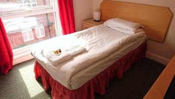 A single bed with a wooden headboard, a bedside table with a lamp, and a window with curtains.