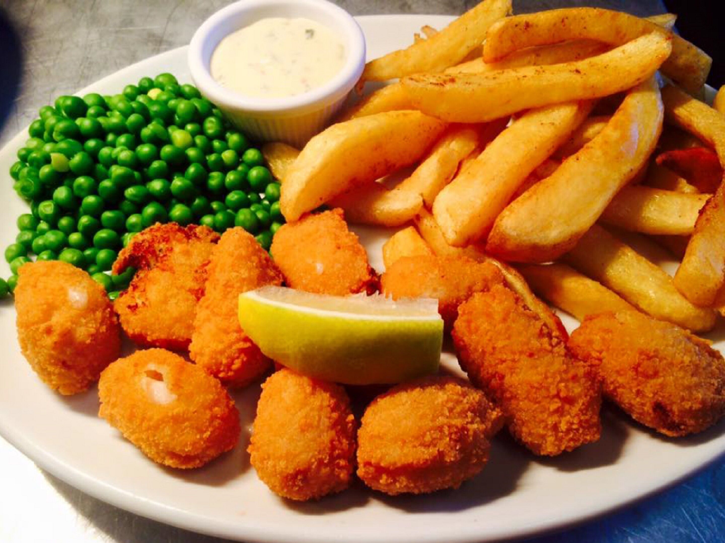 Un plato con pescado frito, papas fritas, guisantes y un pequeño recipiente con salsa.