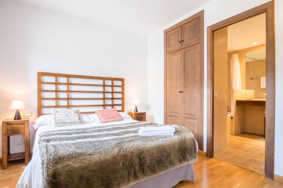 A bedroom with a wooden headboard, a fluffy bedspread, two bedside tables with lamps, and a wooden wardrobe.