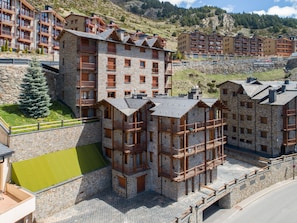 A multi-story stone building with balconies, a ski lift, and a mountainous backdrop.