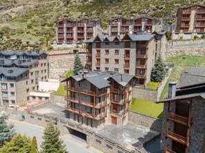 Un hotel de varios pisos con fachada de piedra y balcones de madera, al pie de montañas.